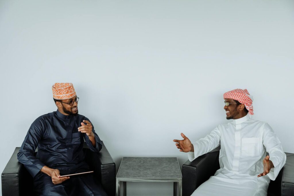 Two men in traditional clothing engaging in a friendly discussion indoors.